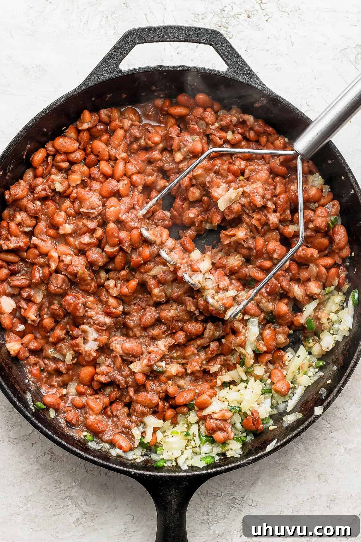 Velvety Frijoles 10 Pinto beans being mashed in a skillet to make refried beans.