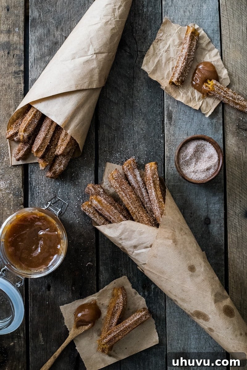 A plate of freshly baked pumpkin churros, generously coated in cinnamon sugar, ready for dipping in a sweet sauce.