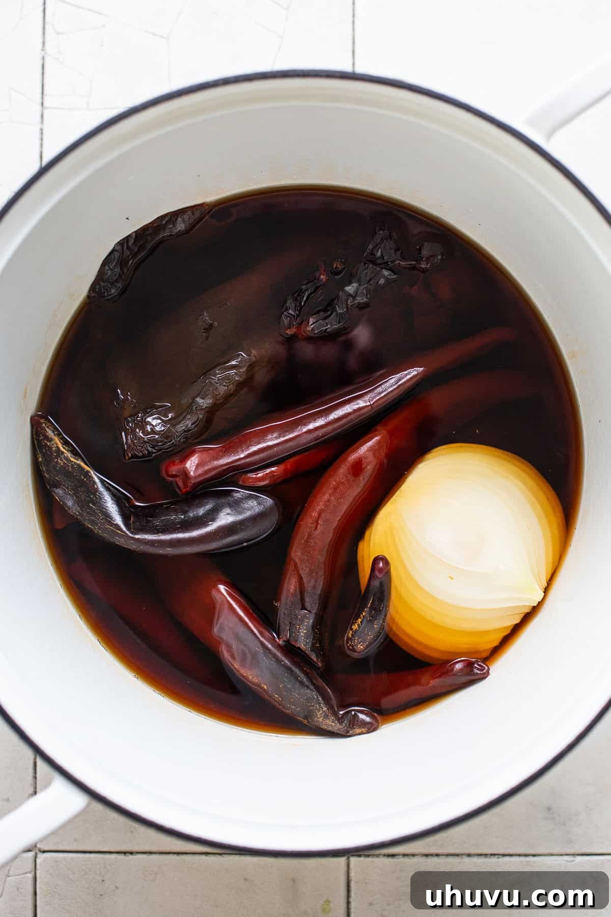 Dried Mexican chiles and an onion soaking in hot water in a pot.