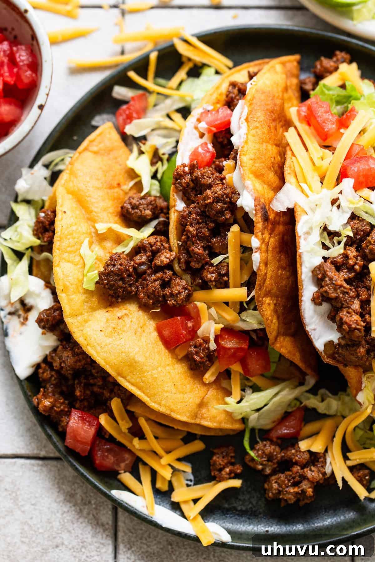 Ground beef tacos ready to eat topped with cheese, lettuce, sour crema, and tomatoes.