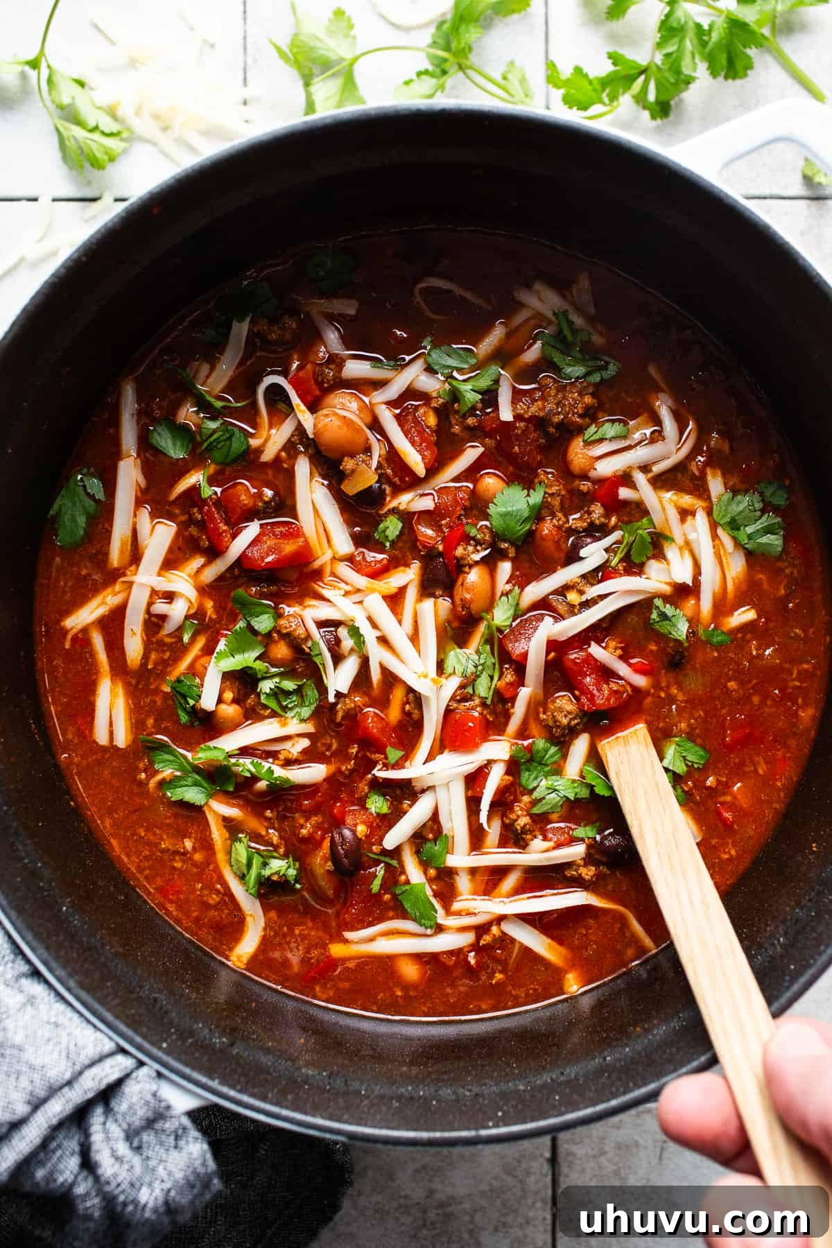 Chorizo Kick Chili 6 A large pot of simmering Chorizo Chili, rich and thick, garnished with fresh cilantro and a sprinkle of shredded cheese, ready to be ladled into bowls for a delicious and comforting meal.