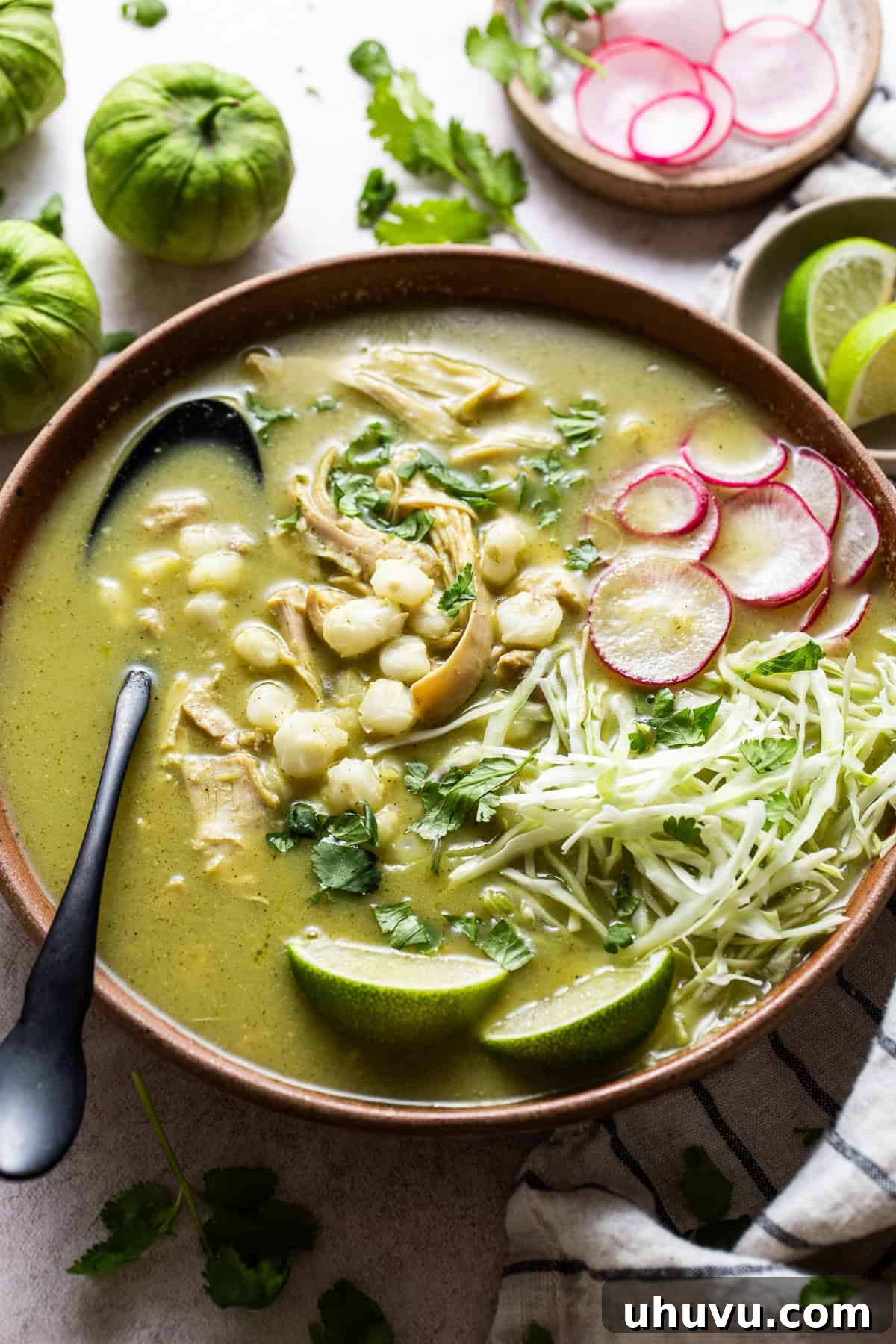 Vibrant Green Pozole 9 A warm bowl of homemade green chicken pozole verde topped with thinly sliced radishes, chopped cilantro, lime wedges, and shredded cabbage.