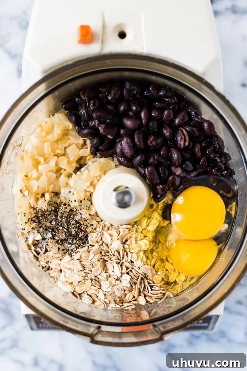 Various fresh ingredients for black bean patties laid out on a surface, including black beans, oats, onions, garlic, and a jalapeño pepper.