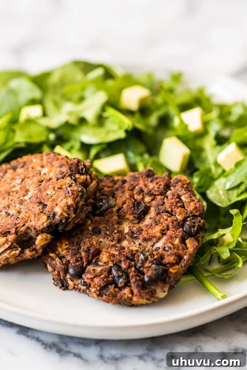Two golden-brown black bean patties served on a plate with a side of fresh green salad and a wedge of lime.
