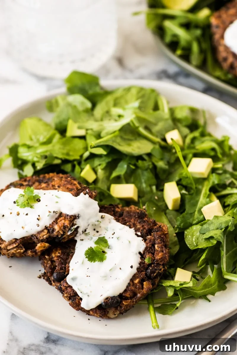 Black bean patties artfully arranged on a plate, generously topped with a creamy, vibrant green cilantro yogurt sauce, ready to be enjoyed as a meal.