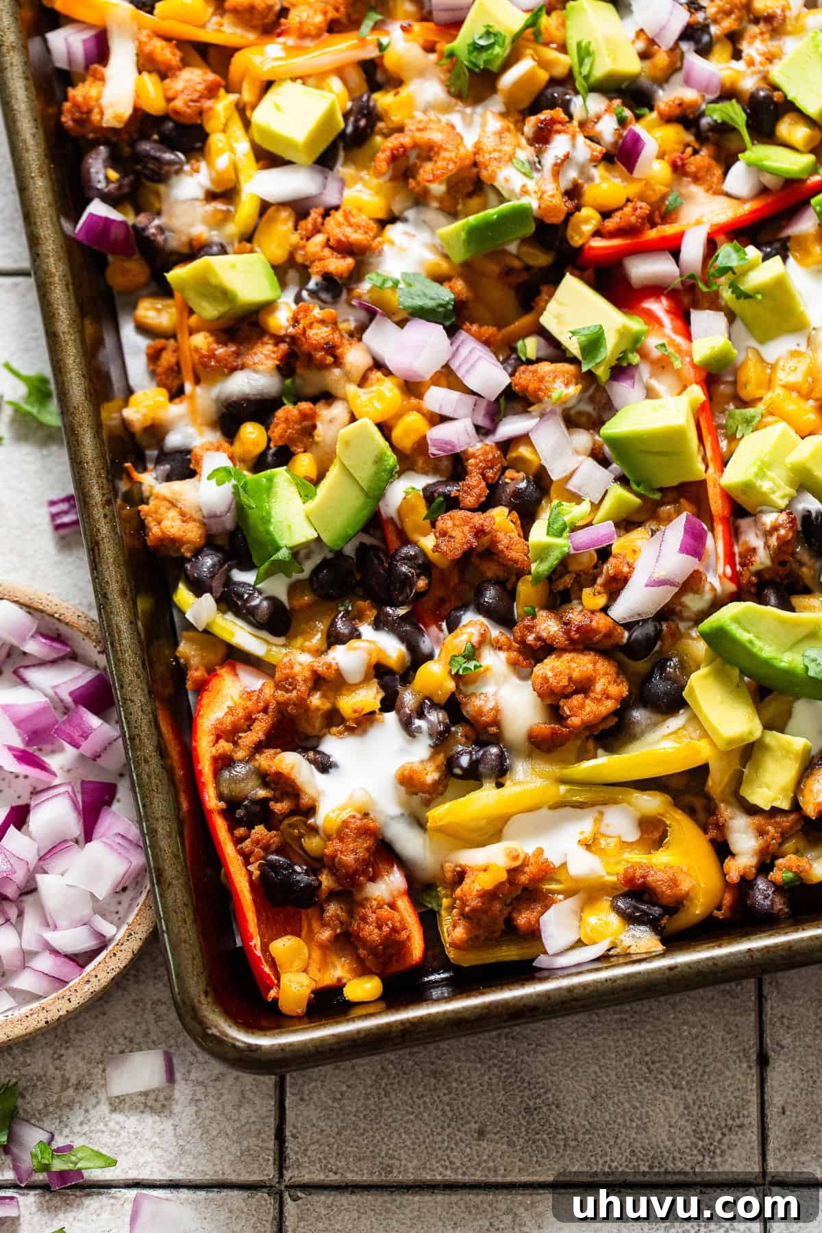 Rainbow Pepper Nachos 8 Finished bell pepper nachos on a sheet pan, adorned with fresh diced avocado, red onion, cilantro, and a creamy sauce, ready for immediate enjoyment.