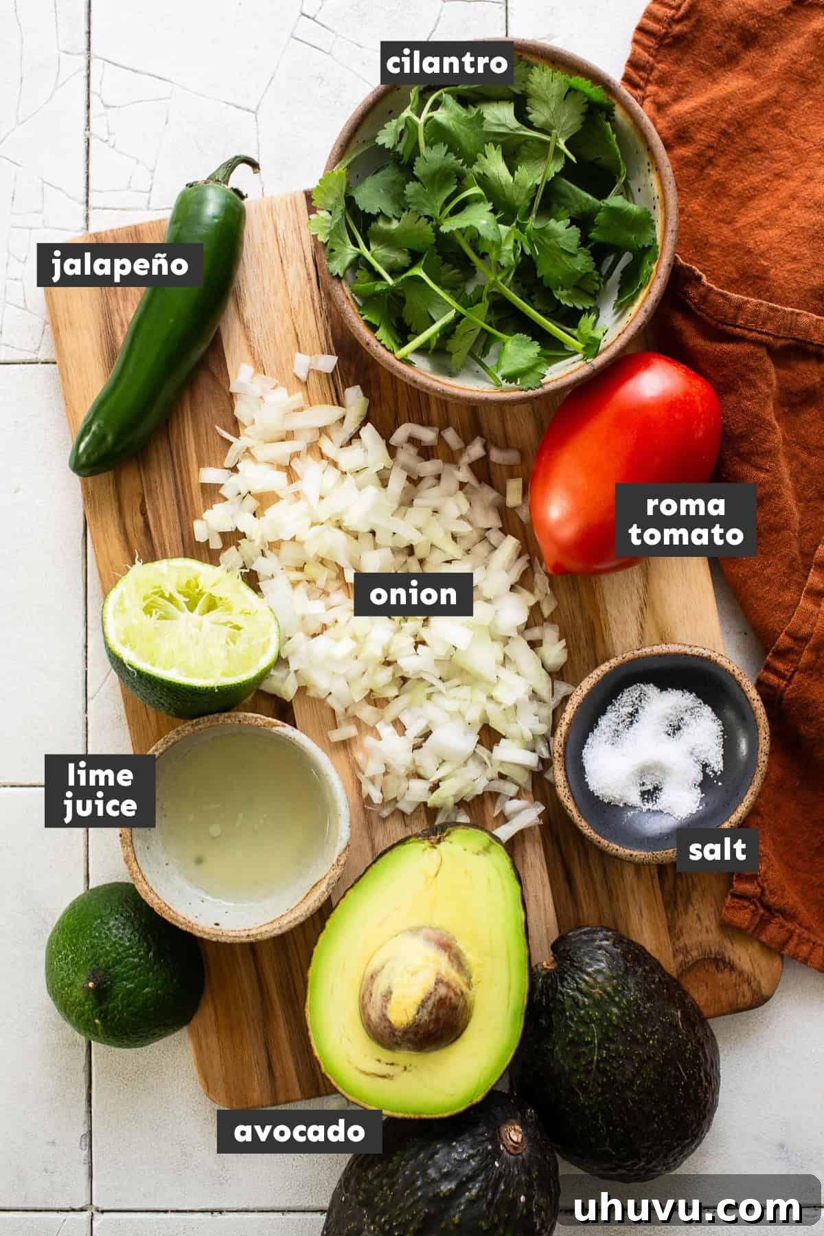 Perfect Guacamole 3 Fresh ingredients for guacamole laid out on a table, including avocados, cilantro, tomatoes, onion, lime, and jalapeño.