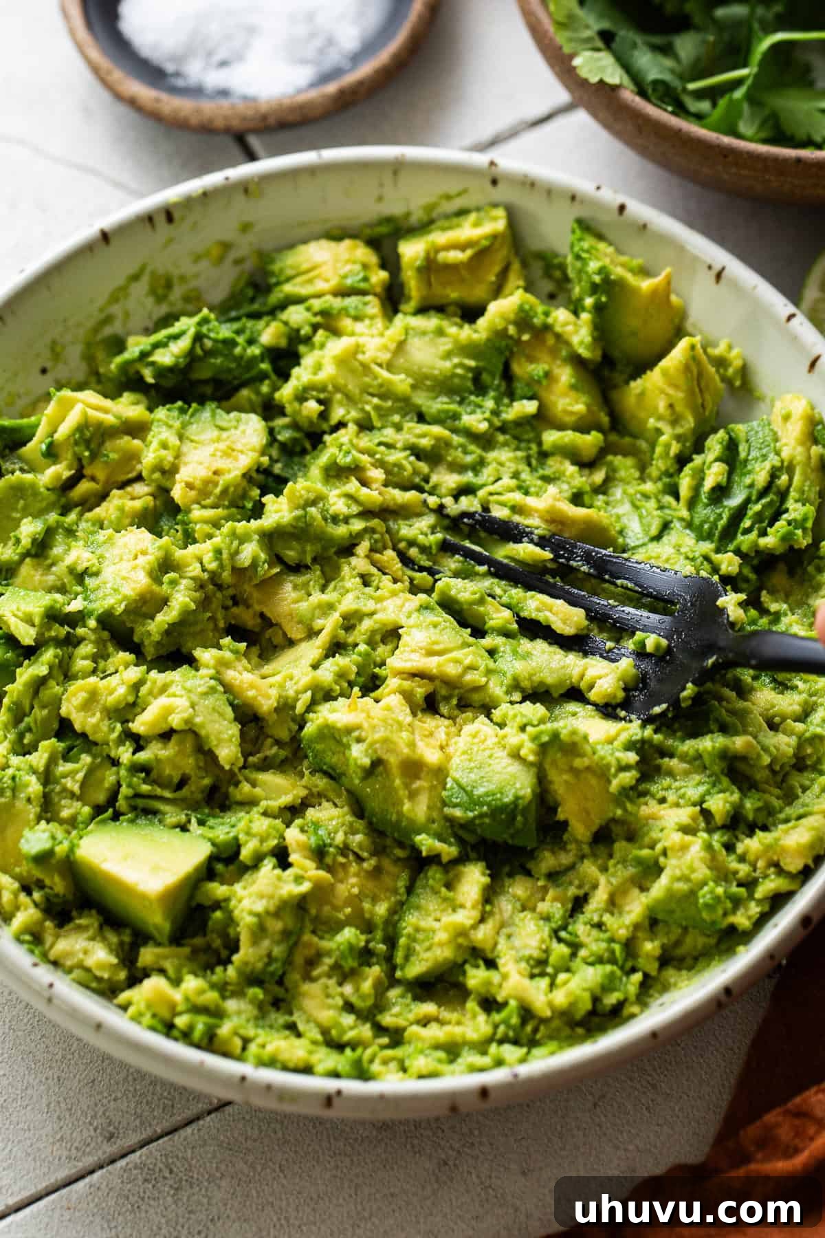 Perfect Guacamole 4 Smashed avocado in a bowl with a fork, showing creamy texture.