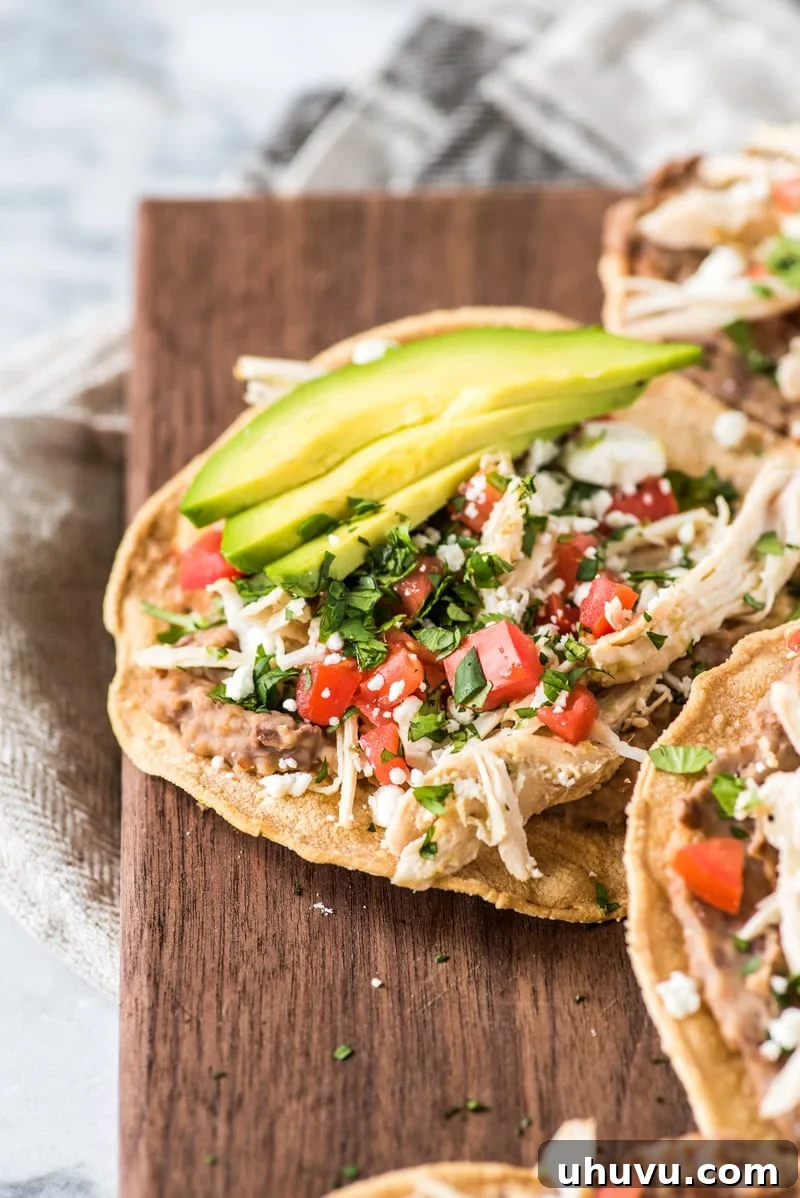 These crispy and crunchy Slow Cooker Salsa Verde Chicken Tostadas are topped with a layer of delicious refried beans, salsa verde chicken, tomatoes, cilantro queso fresco and avocados.
