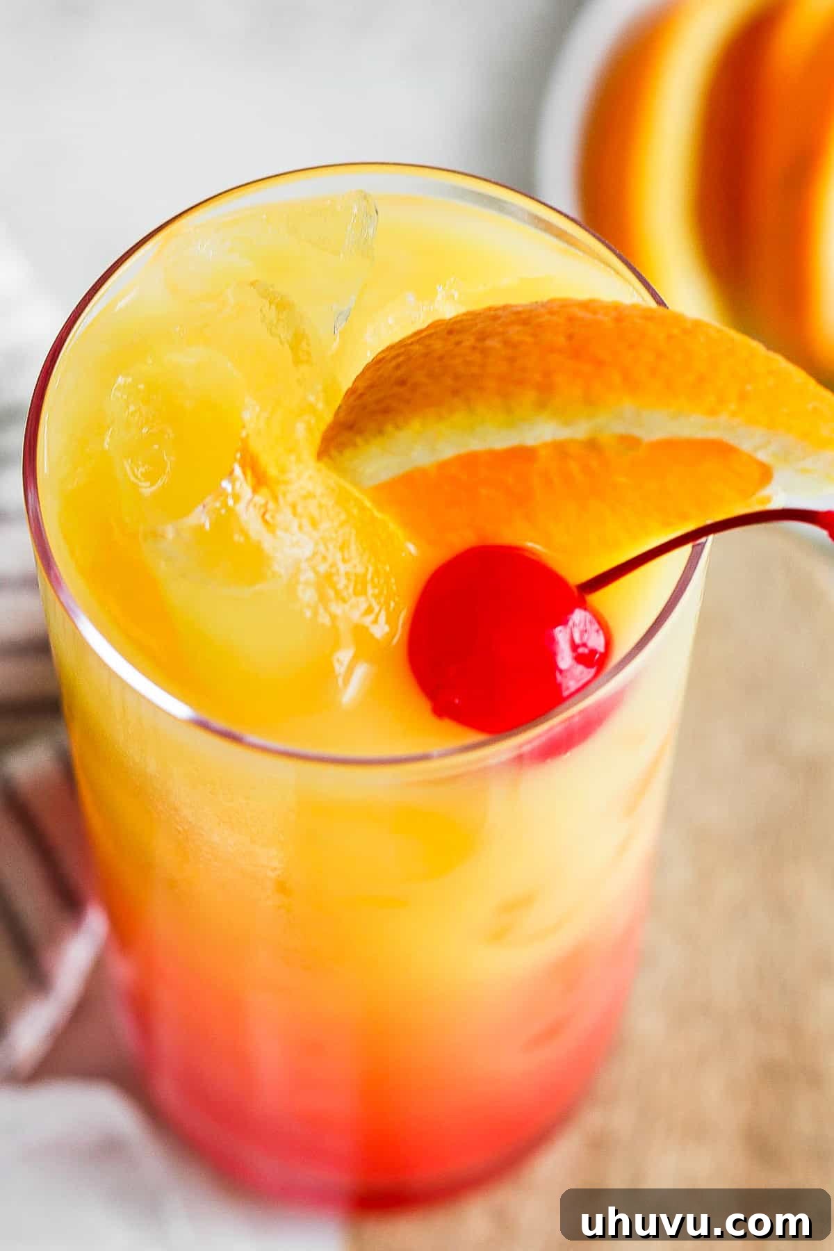 Liquid Dawn 7 A beautifully garnished Tequila Sunrise cocktail with an orange slice and a maraschino cherry, ready to be enjoyed.