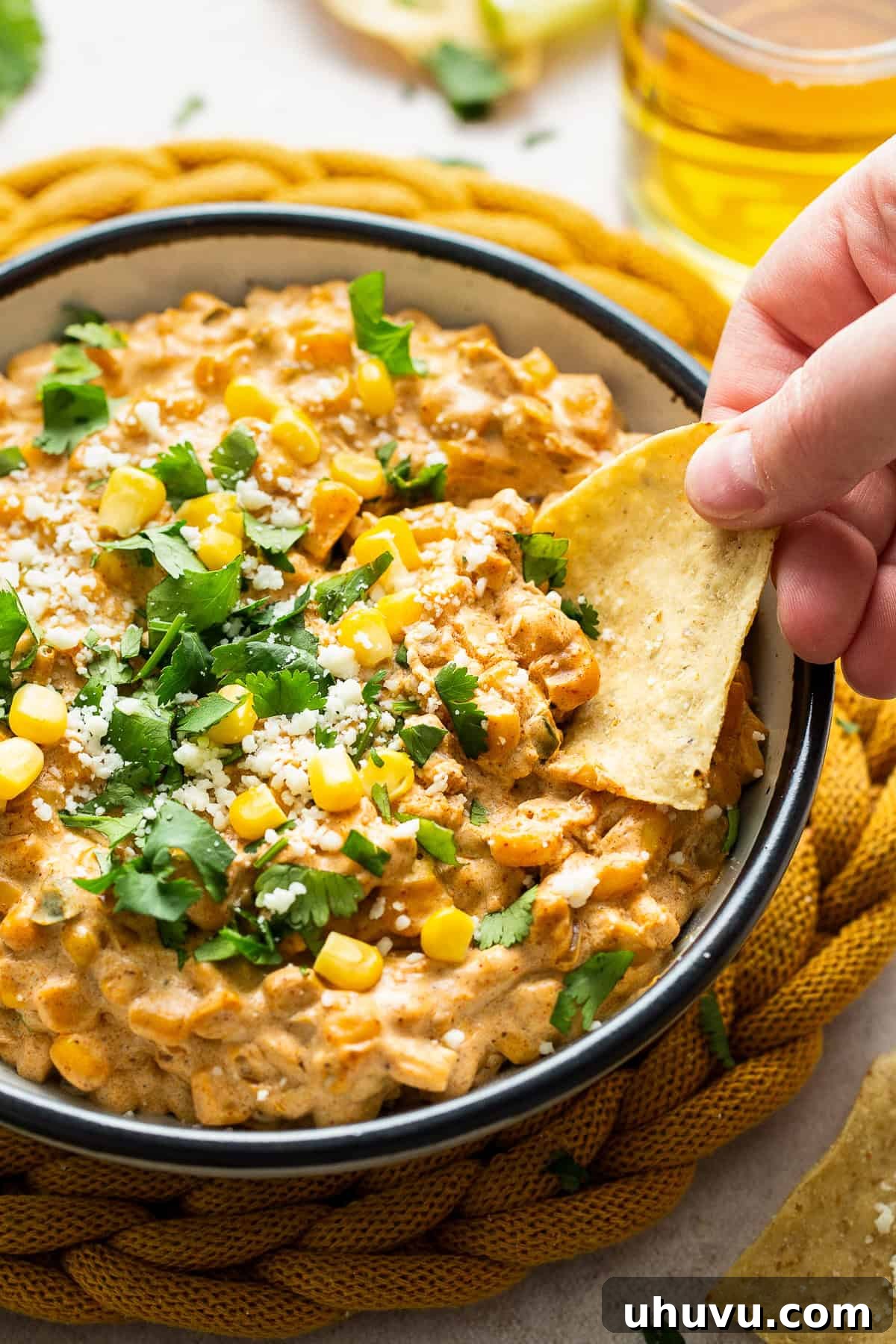 Elote Fiesta Dip 6 A tortilla chip being dipped into a luscious bowl of warm Mexican street corn dip, showing its creamy texture.