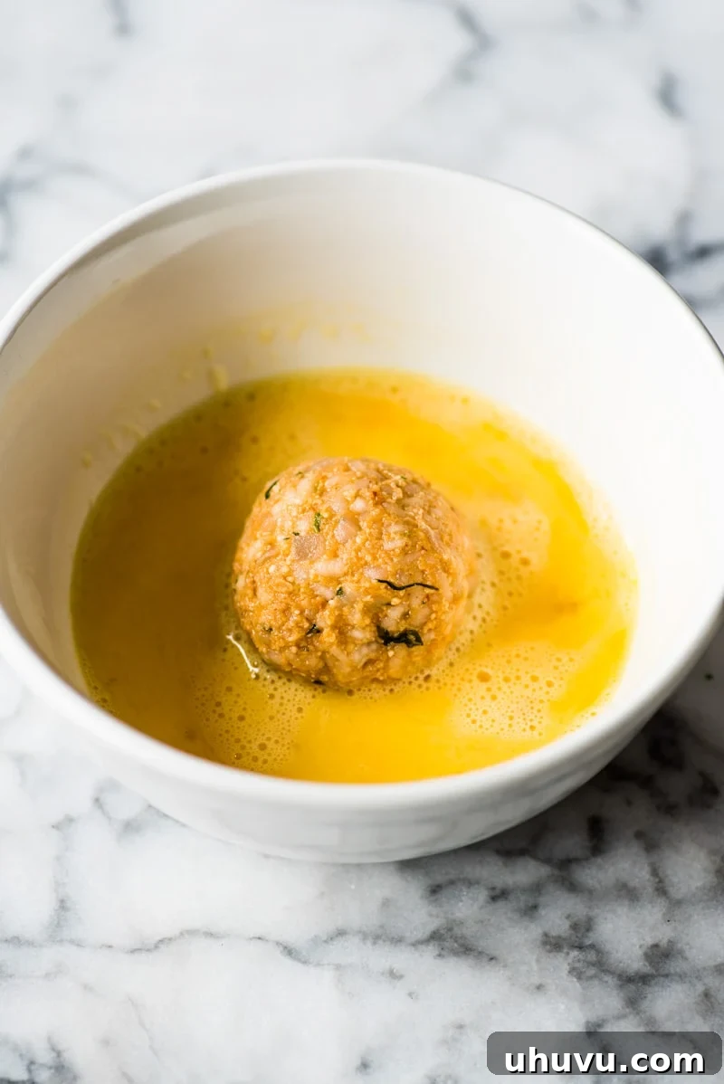 Zesty Fiesta Rice Bites 6 Dipping the cheese-filled arancini rice ball into a shallow bowl of beaten eggs, ensuring even coverage.