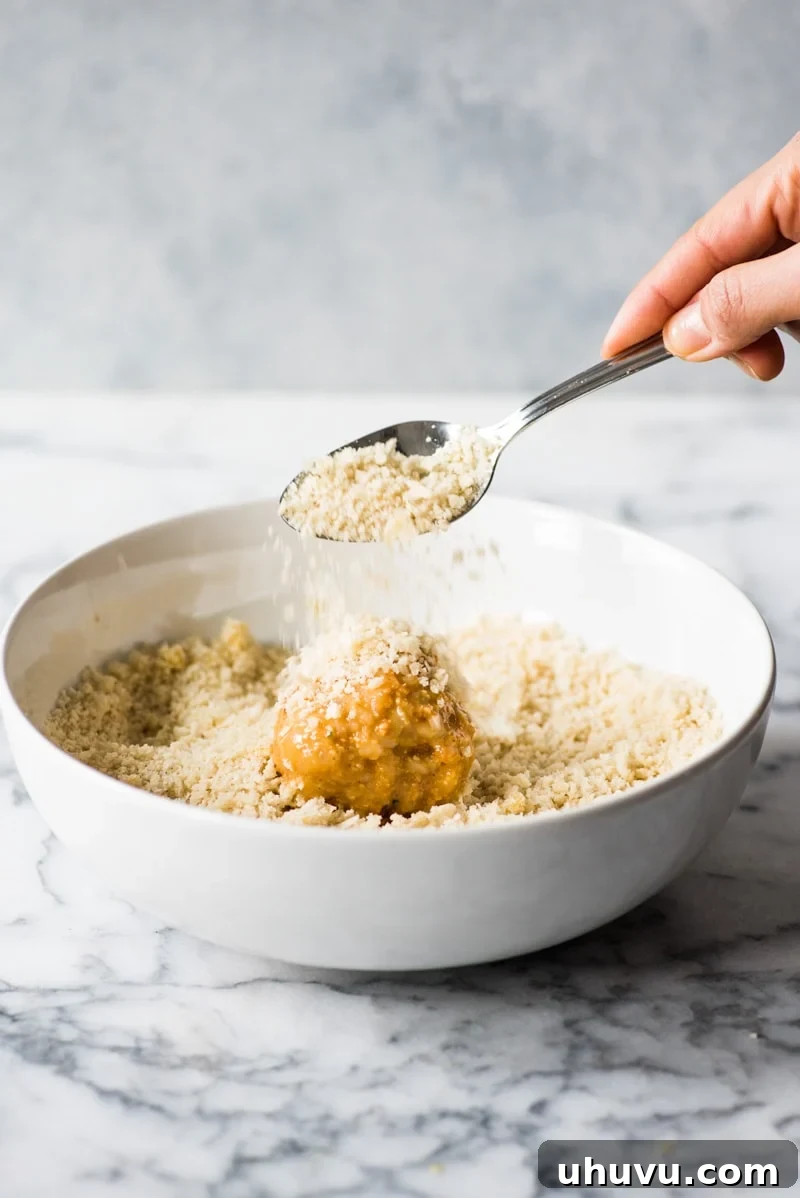 Zesty Fiesta Rice Bites 7 Rolling the egg-coated arancini in a bowl of crunchy panko breadcrumbs, ensuring the entire surface is covered.