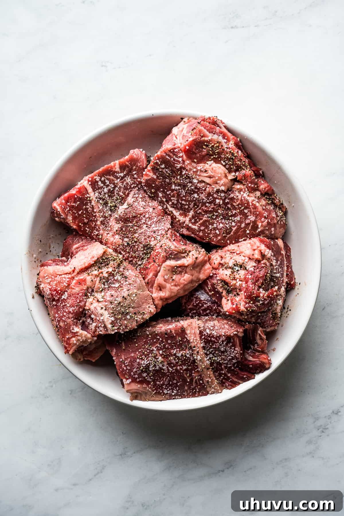 Melt-in-Your-Mouth Barbacoa 4 Beef chuck roast cut into approximately four-inch pieces and generously seasoned with salt and pepper in a mixing bowl.
