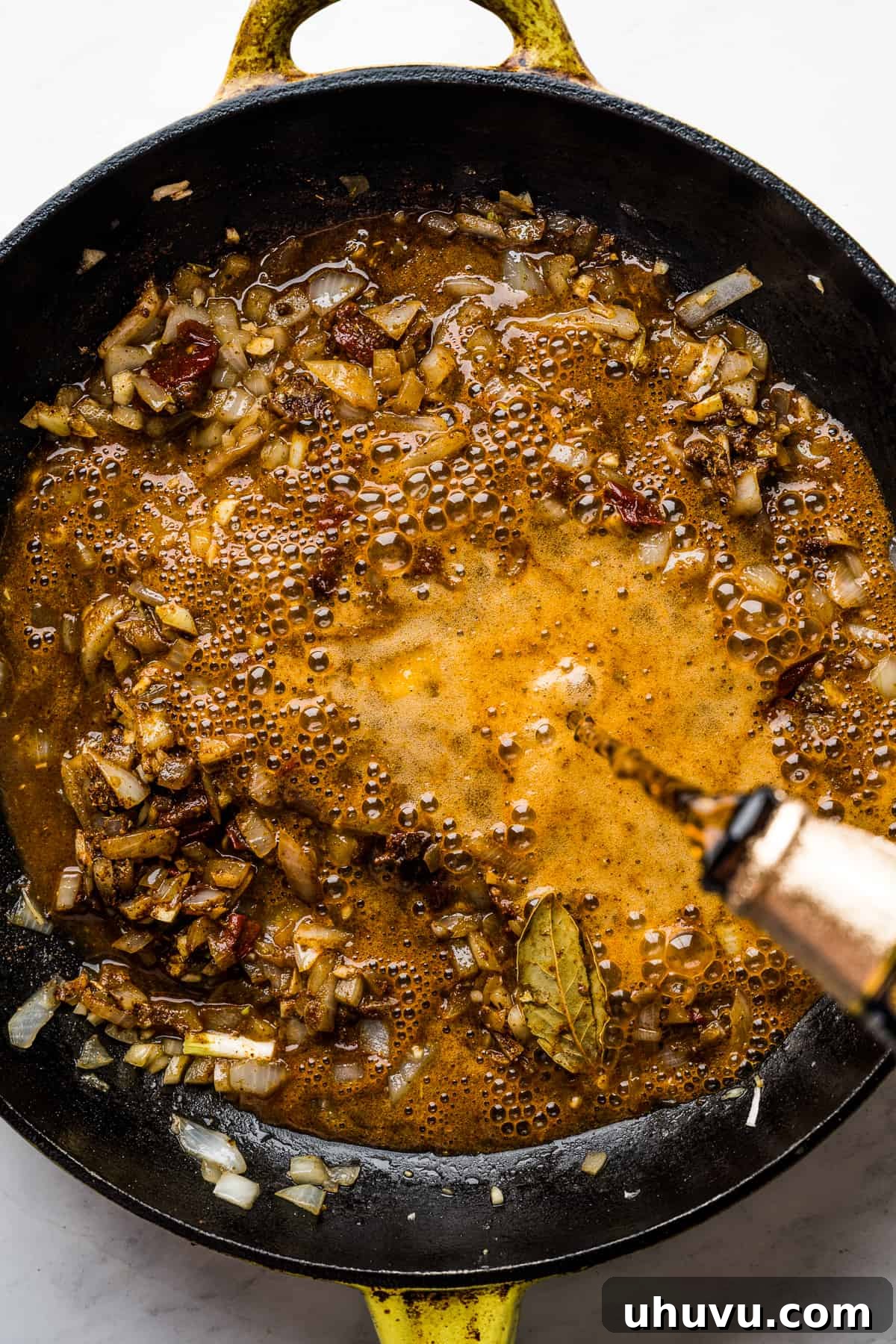 Melt-in-Your-Mouth Barbacoa 7 Dark Mexican beer being added to the skillet containing cooked onions, garlic, apple cider vinegar, lime juice, various spices, and chipotle peppers in adobo sauce.
