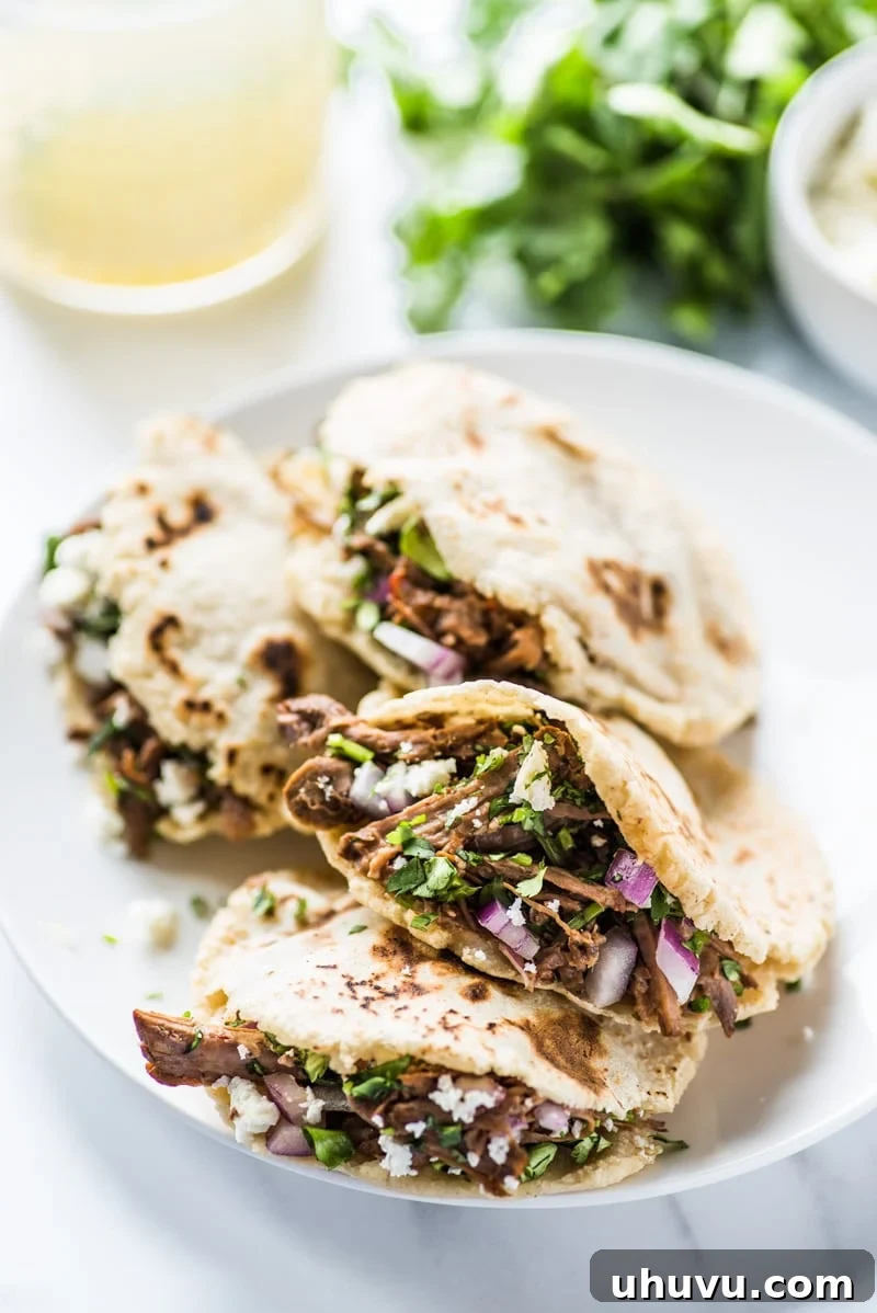 Homemade Gorditas: Authentic Mexican Stuffed Corn Cakes 12 Gorditas filled with shredded beef on a white plate.
