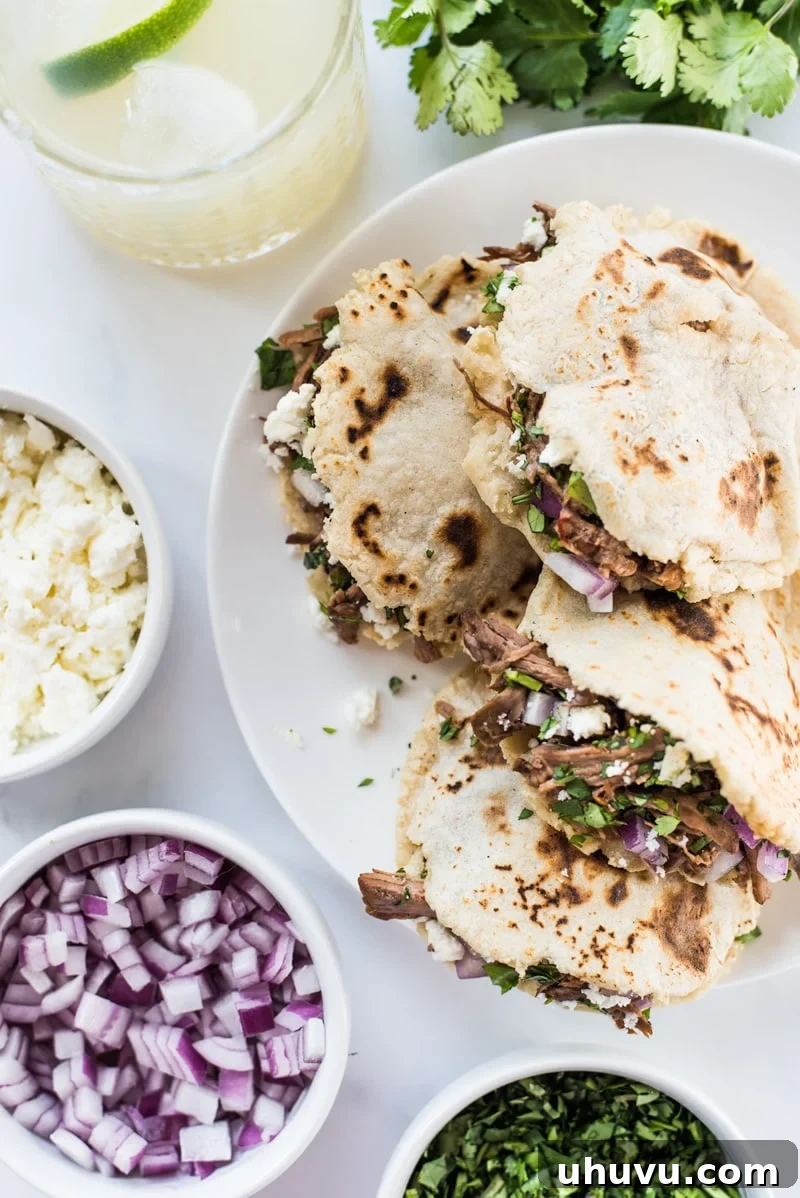 Homemade Gorditas: Authentic Mexican Stuffed Corn Cakes 13 Gorditas on a white plate stuffed with shredded meat and cheese