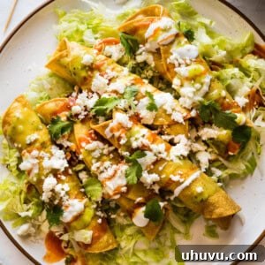 Flautas on a plate topped with crema, hot sauce, salsa verde, lettuce, cilantro, and cotija cheese.