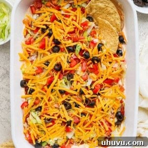 Taco dip in a baking dish topped with shredded cheese, tomatoes, and olive served with tortilla chips.