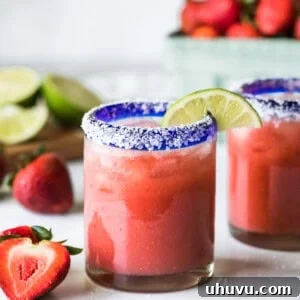 A strawberry margarita in a glass garnished with a lime.