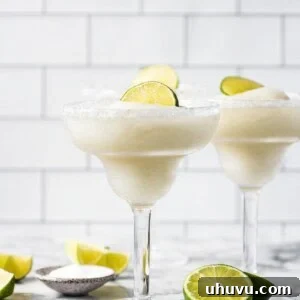 Frozen margaritas in glasses topped with lime wedges.