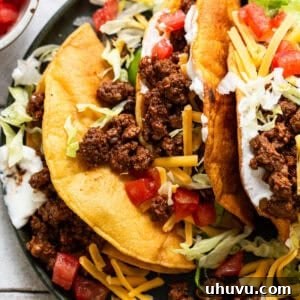 Ground beef tacos ready to eat topped with cheese, lettuce, sour crema, and tomatoes.