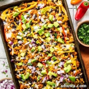 Bell pepper nachos on a sheet pan topped with avocado, onion, cilantro, and other nacho toppings.