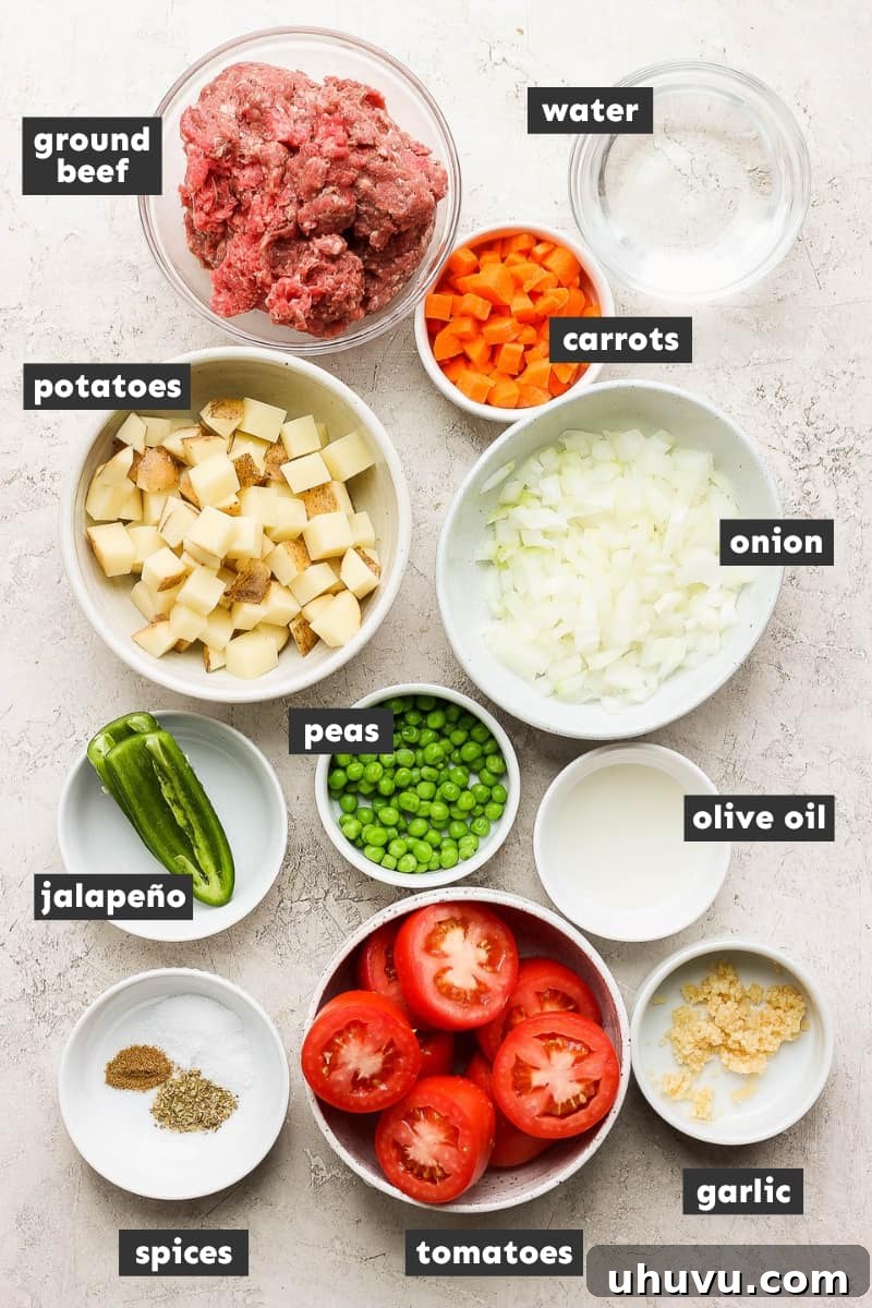 Classic Mexican Beef Hash 3 Fresh ingredients for Mexican picadillo laid out on a wooden table, including tomatoes, onions, garlic, jalapeño, ground beef, potatoes, carrots, and peas.