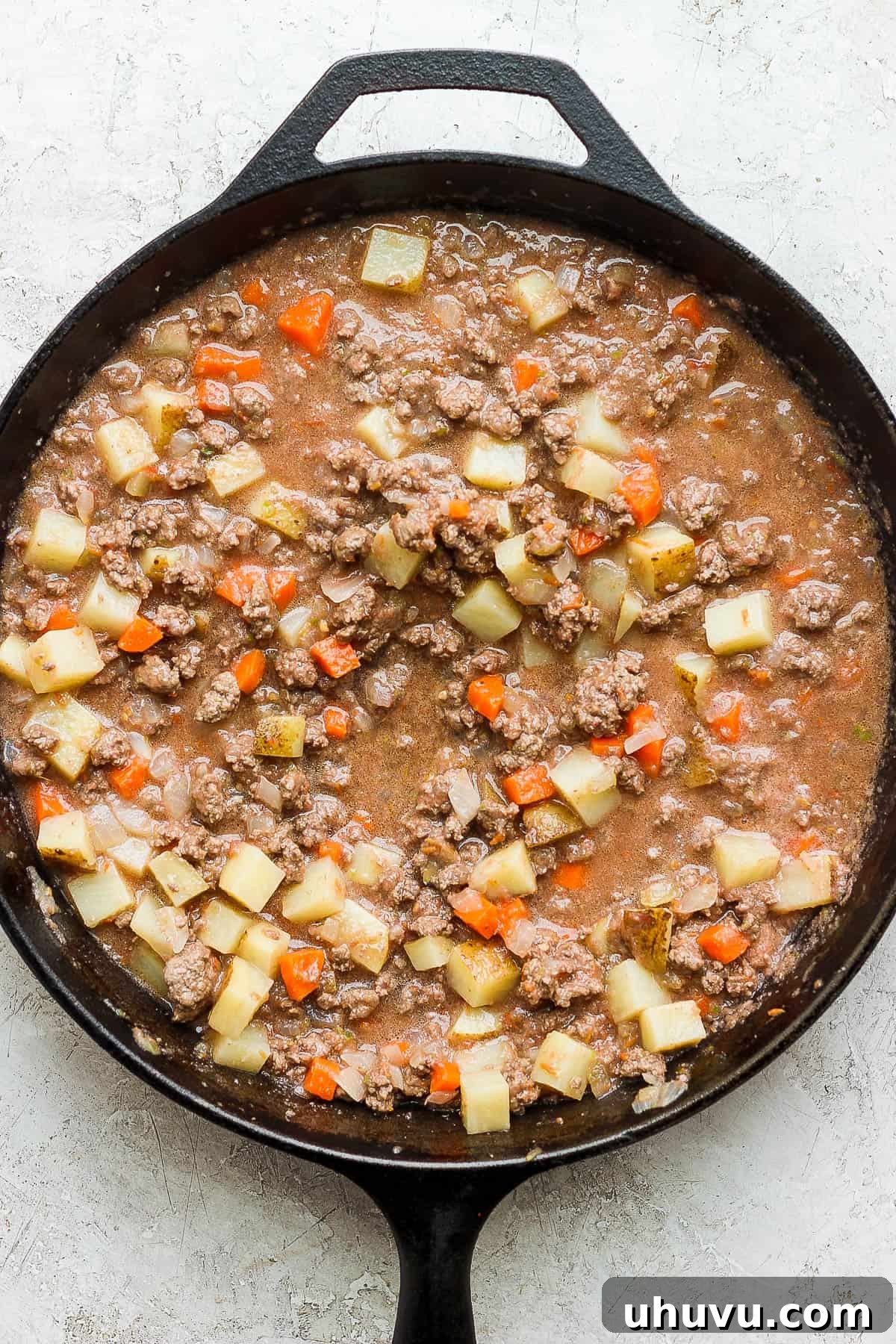 Classic Mexican Beef Hash 8 Mexican picadillo cooking in a skillet, with the sauce bubbling and vegetables softening.
