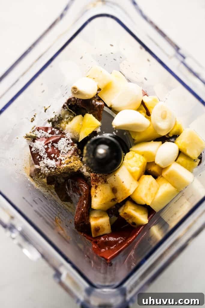 Tacos al pastor marinade ingredients in a blender, showing softened chiles, pineapple, and spices.