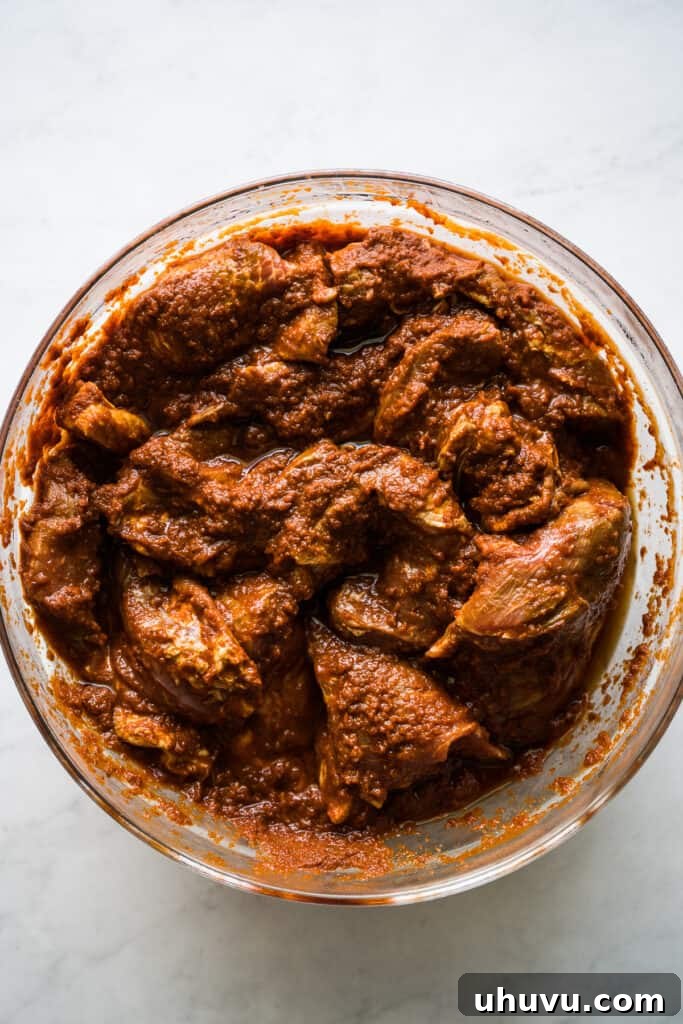 Marinated pork shoulder soaking in a rich, red al pastor marinade in a bowl, ready for cooking.