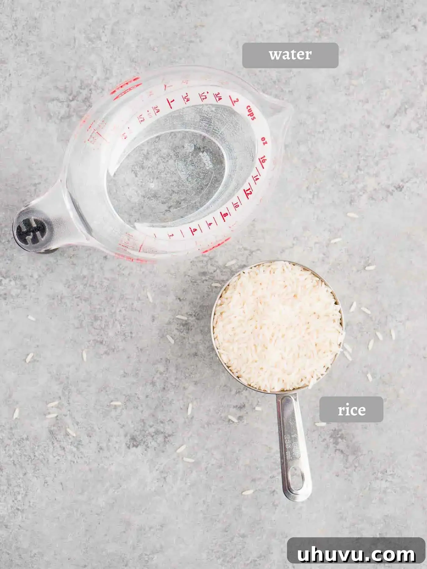 Ingredients for cooking rice laid out: a bowl of white rice and a glass of water on a wooden board.