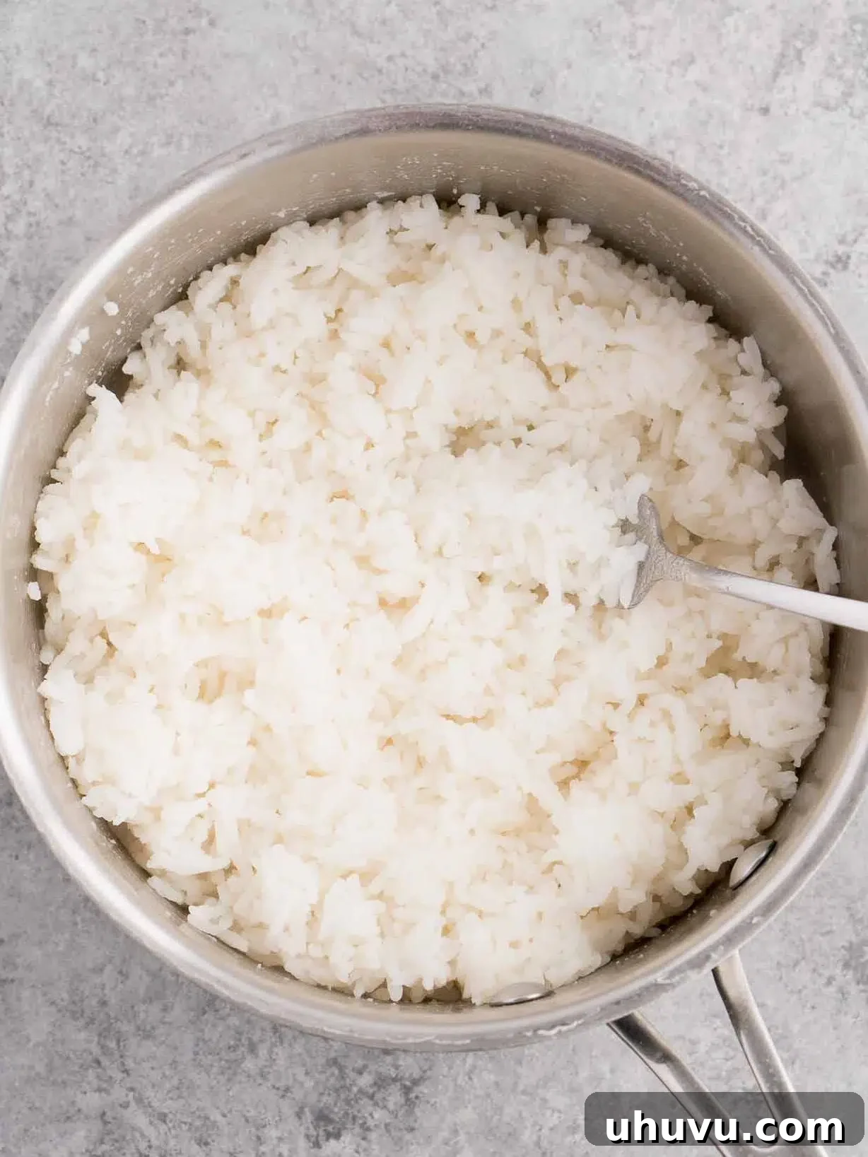 A fork gently fluffing perfectly cooked white rice inside a pot after resting.