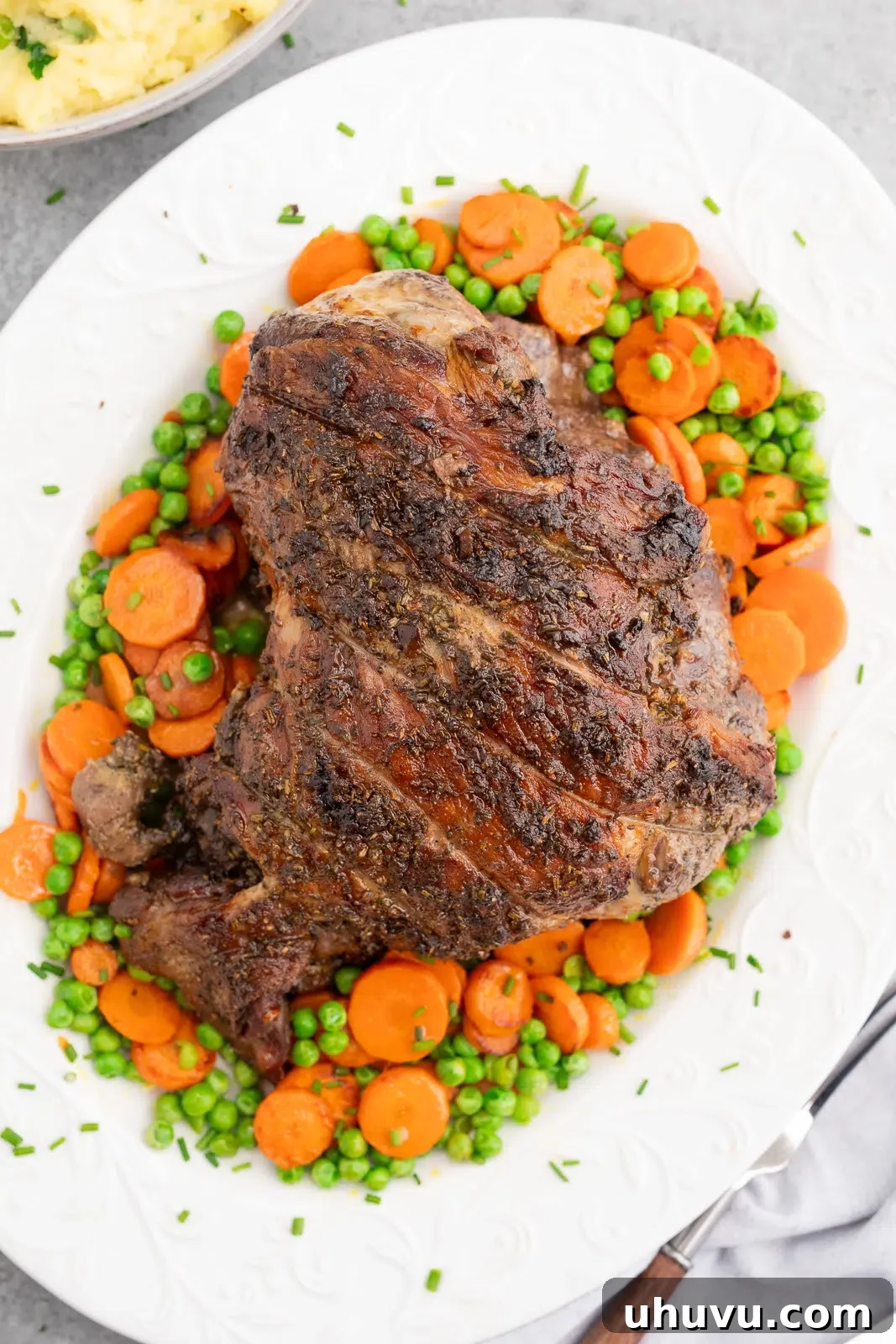 Roasted lamb recipe with garlic and herbs rub served with carrots and peas