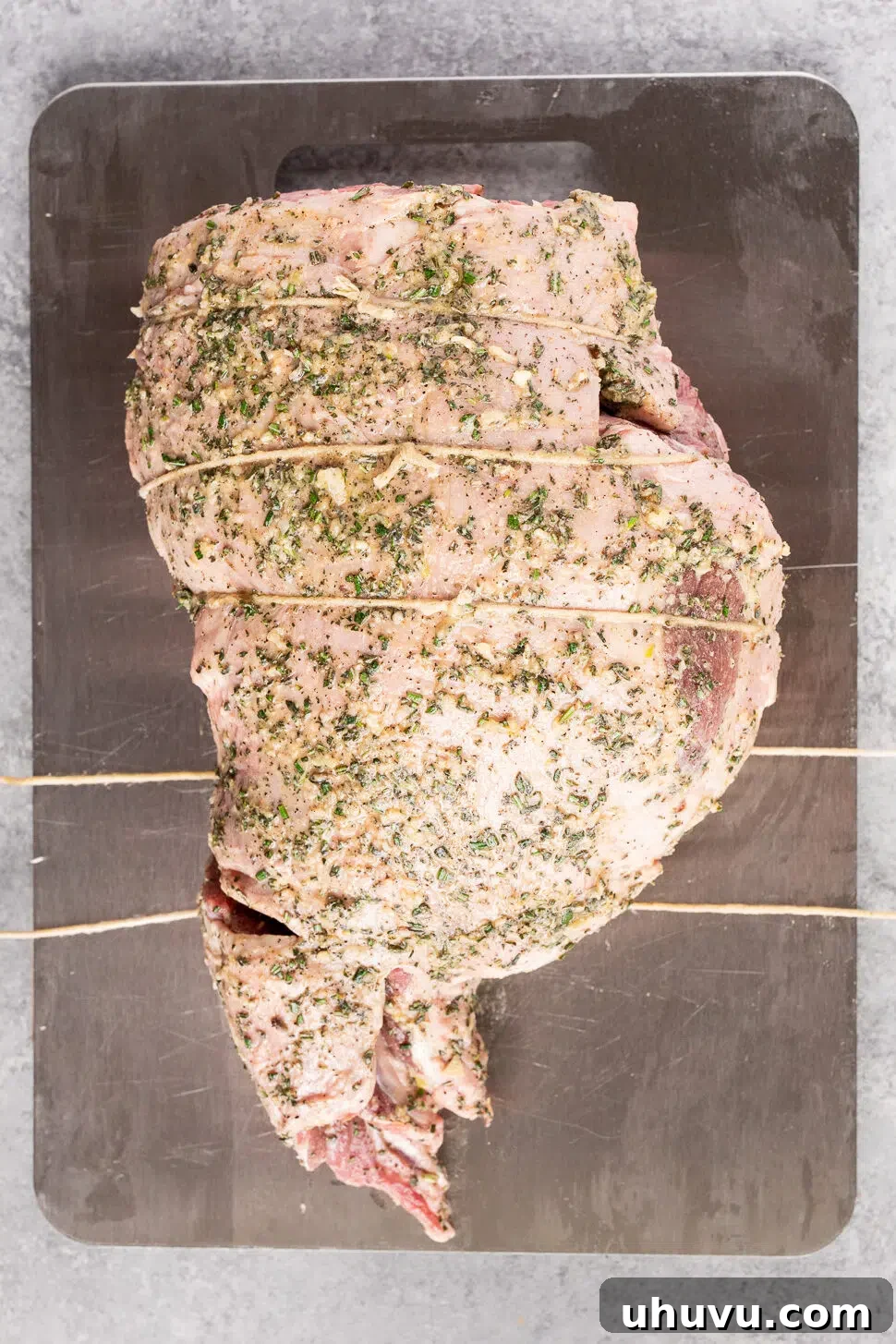 Boneless leg of lamb tied with kitchen twine after being coated with herb garlic rub.