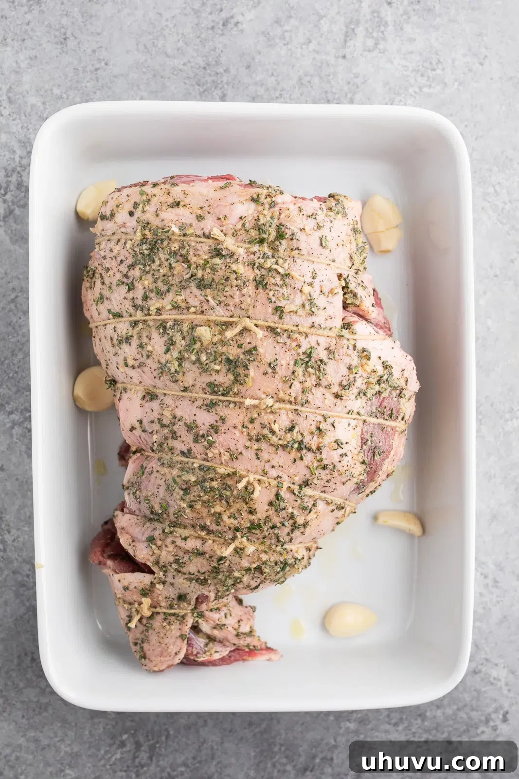 Herb-rubbed boneless leg of lamb placed in a roasting dish before cooking.