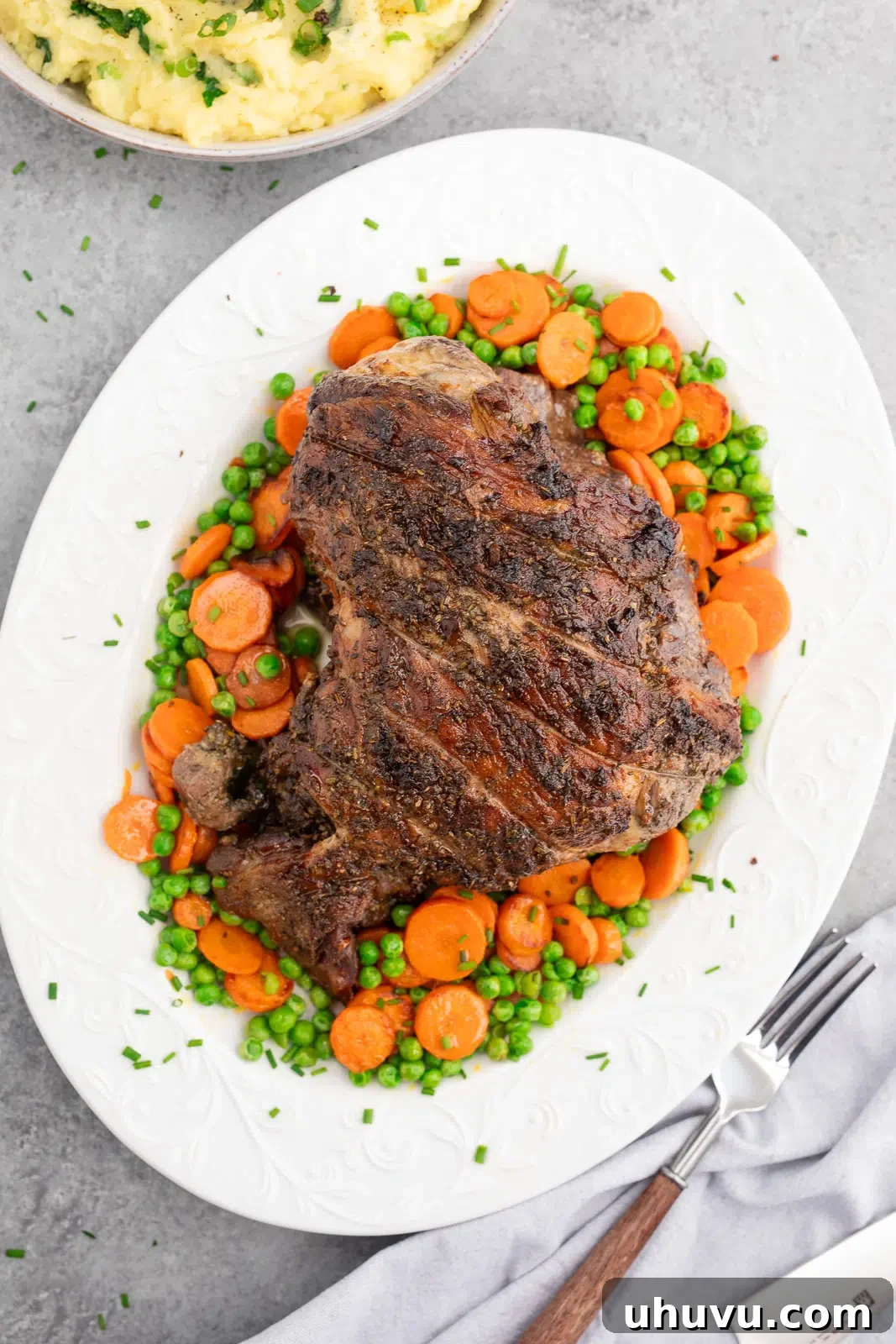 Herb roasted leg of lamb served with carrots and peas on a platter