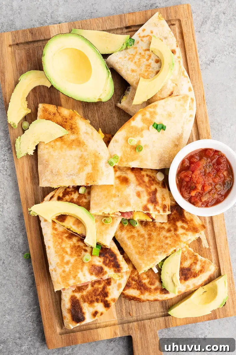 Cheesy Breakfast Quesadillas with Eggs and Salsa 2 savory breakfast quesadillas made with eggs, bacon and cheese on a cutting board