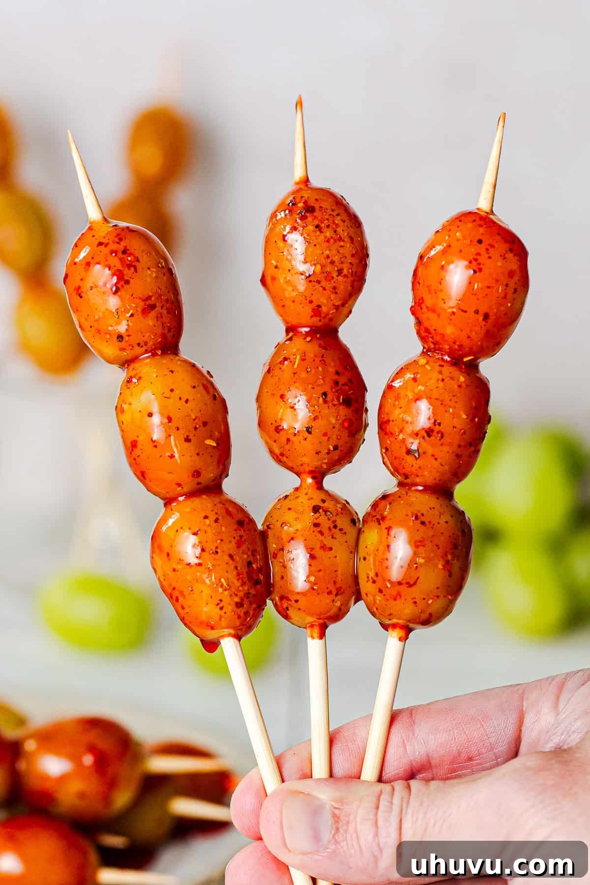 Tequila Chamoy Grapes: Spiked Grapes Recipe 8 Hand holding three skewers of boozy grapes, aka tequila grapes, covered in chamoy and Tajín (chile lime seasoning).
